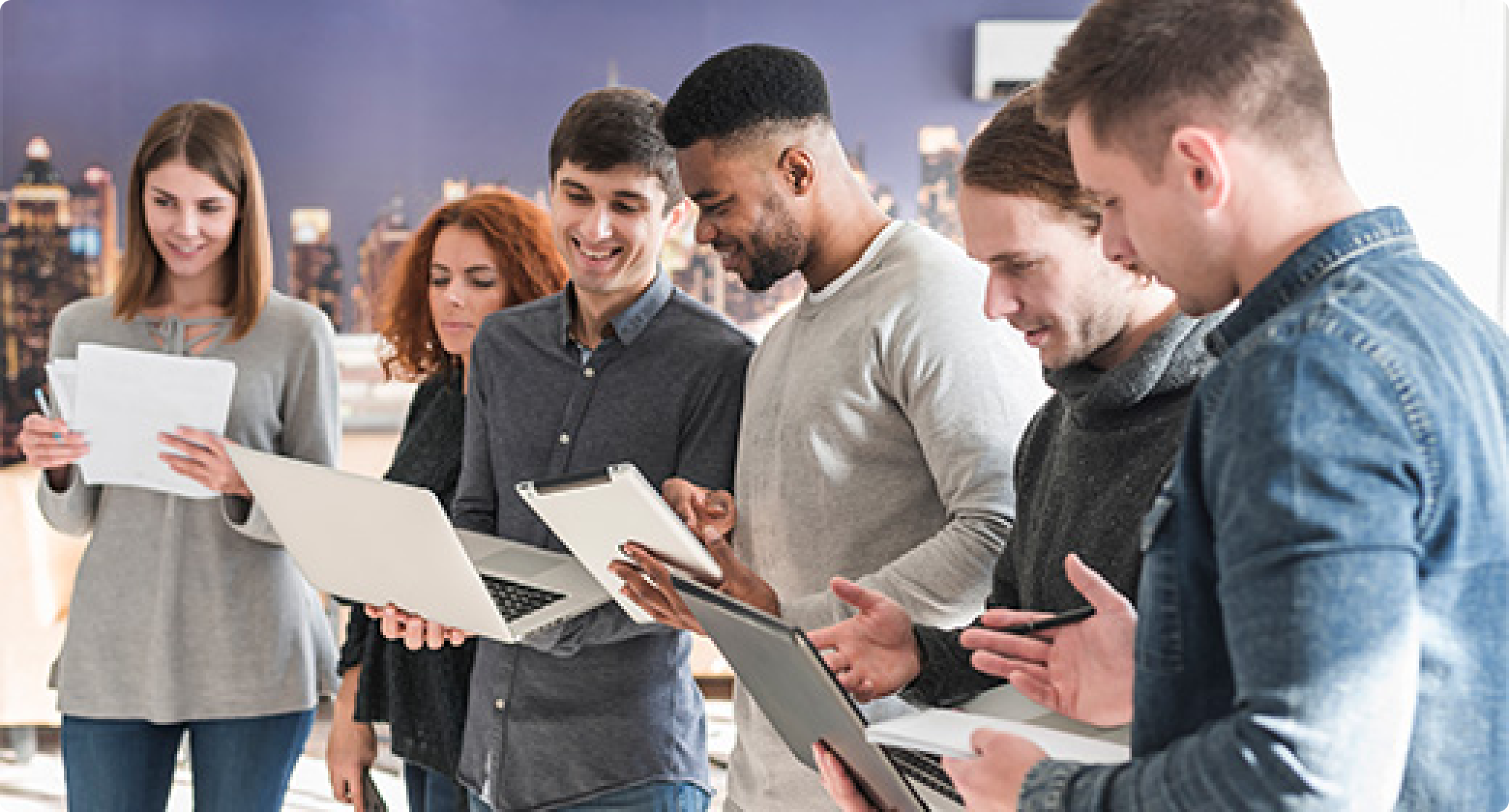 Diverse team of colleagues gathered in an office, collaborating and sharing ideas while working together on laptops and tablet devices.